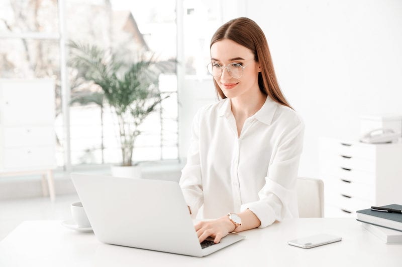 Junge Frau arbeitet lächelnd an ihrem Laptop