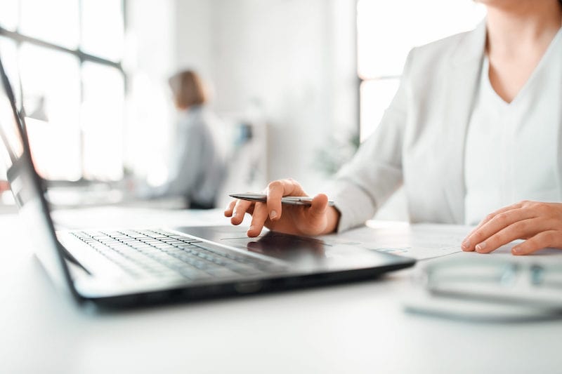 Frau sitzt am Laptop mit Kugelschreiber in der Hand